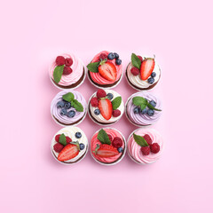 Different delicious cupcakes with cream and berries on pink background, flat lay