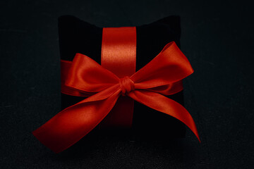 A black small velor gift pillow with a red ribbon tied in a bow