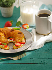 Continental breakfast - coffee, milk, fresh croissant with butter, strawberries, almonds and mint leaves. Healthy lifestyle. Traditional breakfast. Vitamins. Hotel. a restaurant.