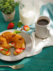 Nicely served breakfast table for one person. Coffee. milk, croissant with fresh strawberries, almonds, mint. Hotel, restaurant, pastry shop, home comfort. Healthy vitamin nutrition.