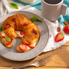 Croissant on a plate with butter, strawberries, almonds, mint leaves and a cup of aromatic black coffee. Tasty breakfast. Vitamins. Healthy lifestyle. A restaurant. hotel, cafe.