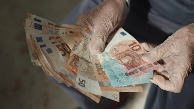 Top view shot of old man hands holding stack of euro banknotes, senior man counting his monthly pension sitting on the armchair. 10, 20 and 50 euro banknotes in hands of elderly man, money budget and