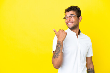 Young handsome Brazilian man isolated on yellow background pointing to the side to present a product