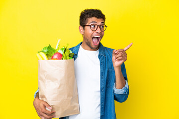 Young Brazilian man holding a grocery shopping bag isolated on yellow background intending to realizes the solution while lifting a finger up