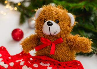 Christmas Teddy Bear sits near a red blanket and spruce branches on a blurry background. Christmas concept.