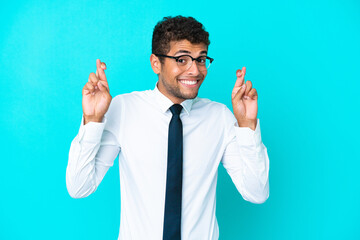 Young business Brazilian man isolated on blue background with fingers crossing