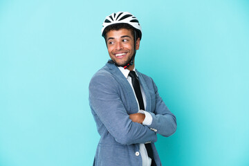 Young business Brazilian man with bike helmet isolated on blue background with arms crossed and happy