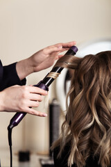 Fototapeta premium Female hands of a hair master. Close-up of blond hair on a curling iron. Curling curls.