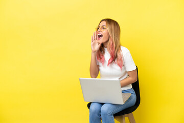 Young woman sitting on a chair with laptop over isolated yellow background shouting with mouth wide open to the side