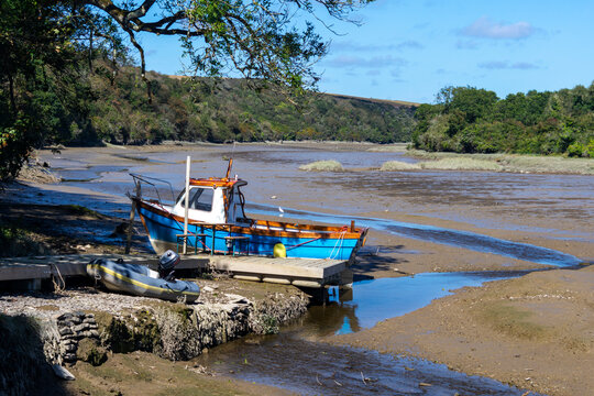 A small fishing boat moored on mud flats near Padstow, Cornwall, England, UK while the tide is out - Powered by Adobe