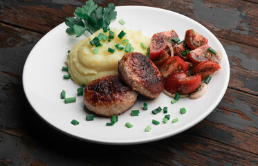 Homemade cutlets with mashed potatoes and fresh cherry tomatoes salad on a wooden background.
