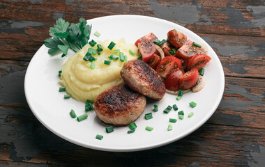 Homemade cutlets with mashed potatoes and fresh cherry tomatoes salad on a wooden background.