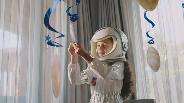 Fantasy child astronaut playing with suspended cosmic planets.Girl astronaut in the form in a bumblebee astronaut costume is playing a room space in her children's room,interior is hung with planets.