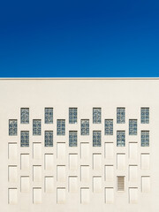 Rectangular windows and niches in the outer wall of the building against blue sky. Architectural elements repeating pattern of the modern built structure. Geometric exterior wall detail.