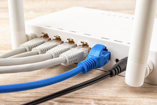 Blue and gray network cable plugs connected to the white Wi-Fi wireless router on a wooden desk. Close-up of home or office wlan router provides an internet connection. Internet hardware concept.