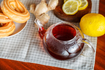 A cup of strong infused tea on a napkin next to lemon ginger jam and donuts.