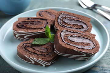Tasty chocolate cake roll with cream and mint on blue wooden table, closeup
