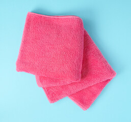 Two pink terry towels close-up on a light blue background.