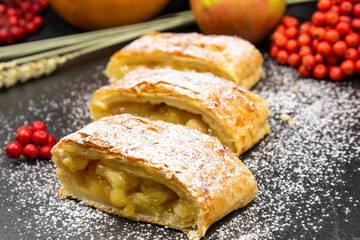 Strudel with apples. A wonderful dessert made of puff pastry. Black background.