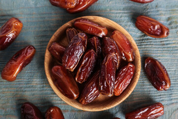 Sweet dried dates in bowl on light blue wooden table, flat lay