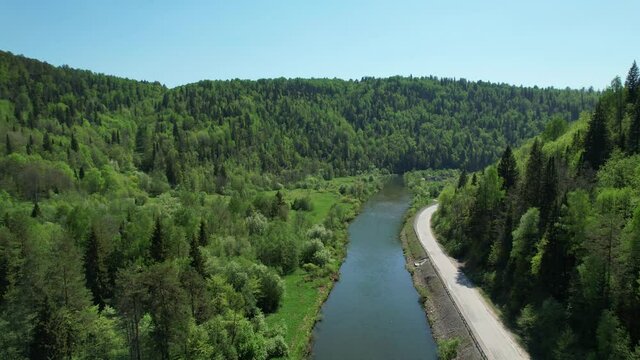 Picturesque nature in summer. The river is parallel to the road on which a white minibus is traveling. Aerial view. Ural nature, Russia.