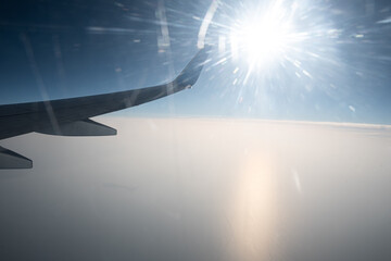 View from the window of a flying plane. Clouds, blue sky and a fragment of the airplane wing.