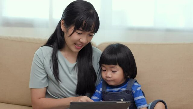 Happy asian family mother and  son using tablet for education. Little boy watching funny social media.  Mom with kid using tablet video call to father.