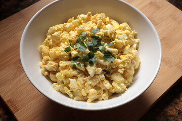 Egg salad with parsley in a white bowl on a bamboo wood board