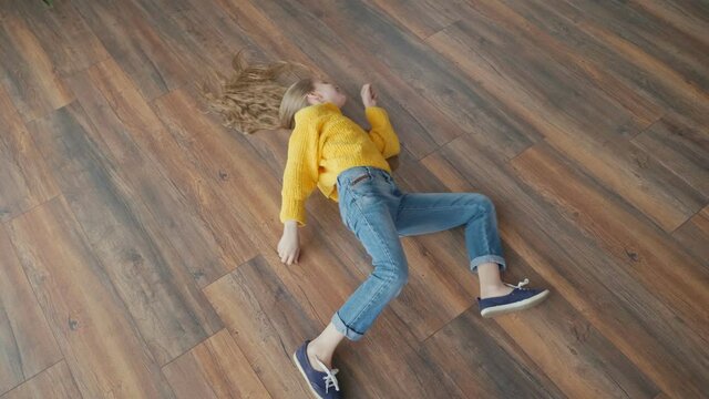 The Energetic Cheerful Teenage Girl is Having Fun, Fooling Around, Making Arbitrary Movements on the Floor of the House. Crazy Movements, Fun, Relaxation, Good Mood. Mental Health. View From Above.