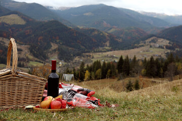 Wicker picnic basket, wine, snacks and plaid in mountains on autumn day, space for text