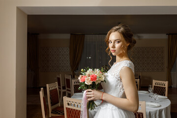 a young beautiful bride with a bouquet before the wedding in a restaurant at the wedding table