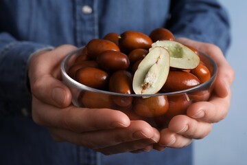 Woman holding glass bowl with fresh Ziziphus jujuba fruits on light background, closeup