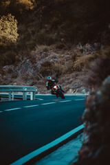 Vertical shot of a biker turning his motorcycle on the highway with high hills