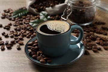 Cup of aromatic hot coffee and beans on wooden table