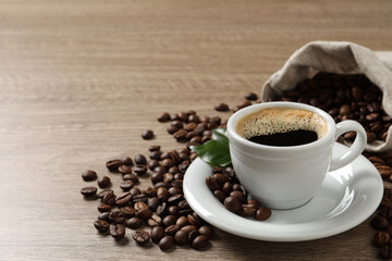 Cup of aromatic hot coffee and beans on wooden table. Space for text