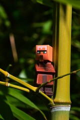 Obraz premium LEGO Minecraft villager figure in brown suit standing on side branch of Phyllostachys bamboo plant near node, partially sunlit by autumn daylight sunshine. 