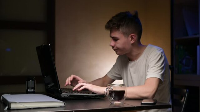 A young man's laptop starts to smoke while he is working. The guy in a panic pours a cup of coffee on the keyboard to extinguish the starting fire