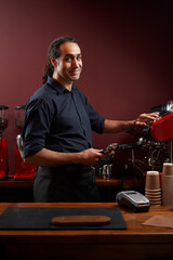 Portrait of a handsome barista in black shirt and apron at the bar of the modern cafe.