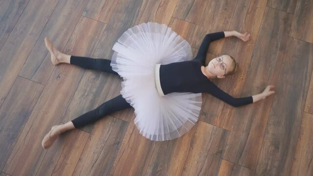 View From Above. A Girl Ballerina in a Tutu Lies on the Floor, Dreamily Looks Up, Making the Movements of a Snow Angel. Playful Mood, Mental Health.