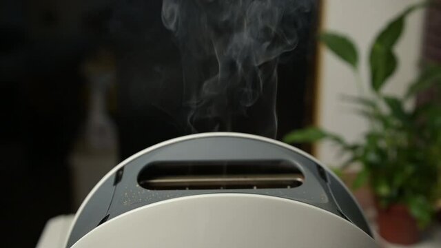 Burnt slices of bread fly out of the toaster slowly. Toaster smokes and fires burnt toast