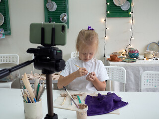 Girl vlogger recording video with modelling clay and speaking for smartphone camera. Kid blogger in...