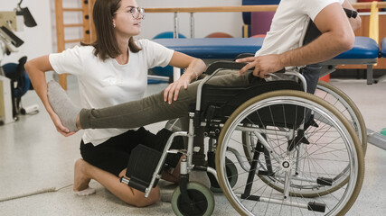 Female physiotherapist and male patient seated in a wheelchair during rehabilitation treatment -...
