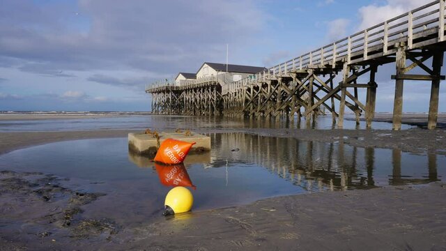Boje &bdquo;Schwimmen verboten&ldquo; vor Pfahlbauten in St. Peter Ording an der Nordsee im Wattenmeer