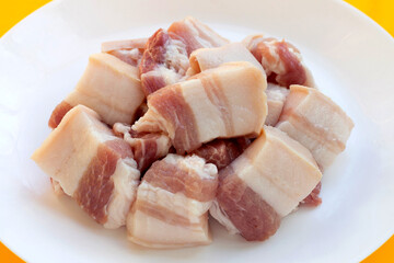 Streaky pork in white plate on yellow background.