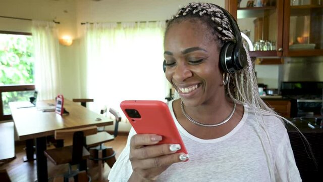 mujer afroamericana muy feliz escuchando m&uacute;sica con aud&iacute;fonos con su celular