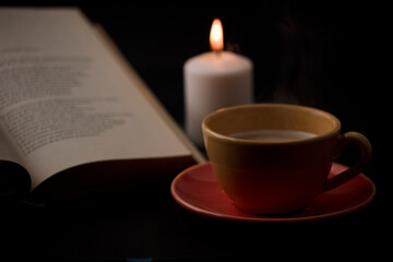 cup of tea with hot smoke and lit candle. on the desk at home, power outage (focus on cup).