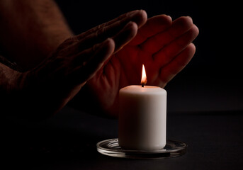 Obraz na płótnie Canvas Isolated burning candle with man's hands warming up with the heat of the fire, black background.