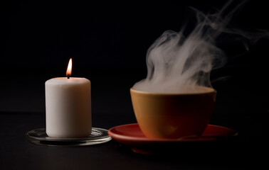 cup of tea with hot smoke and lit candle. on the desk at home, power outage (focus on lit candle).