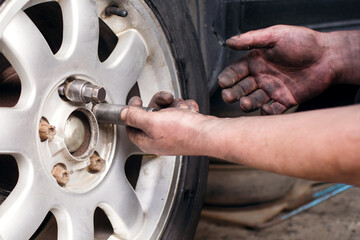 A mechanic at a service station replaces a car wheel, a worker's hands in black fuel oil and a tool for unscrewing bolts close-up near the wheel. Tire service, workflow