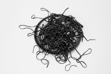 Black tangled pasta in a black plate on a white table with black cutlery